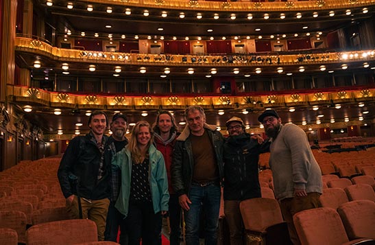 A group of people smile at the camera, standing inside a large indoor theatre.