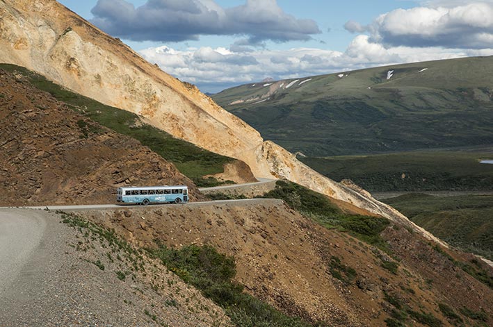 A blue bus wraps around dark orange cliffs.