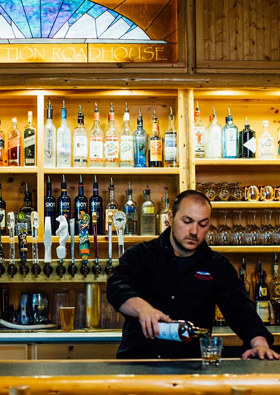 A bartender pours a drink at a rustic wooden bar.