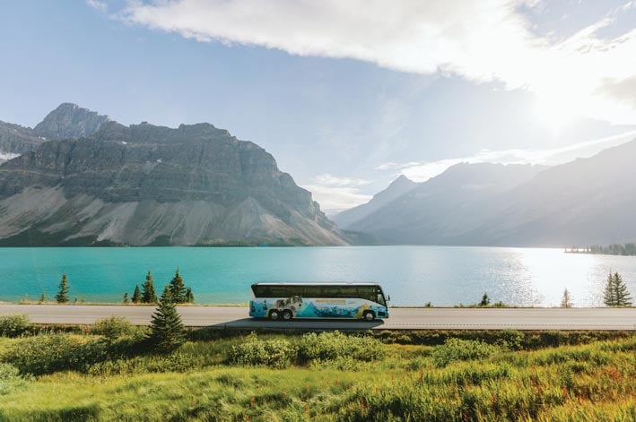 A bus drives alongside a crystal blue lake.
