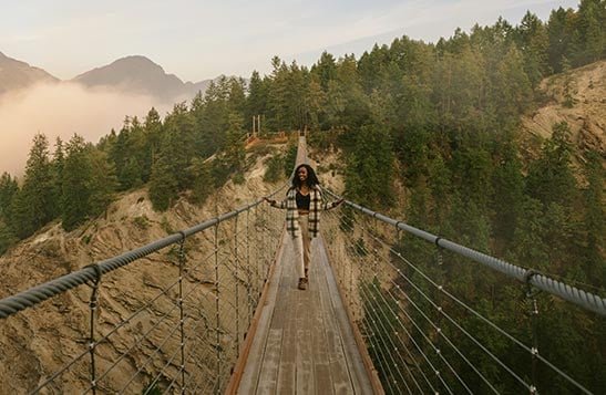 A person walks on a narrow suspension bridge over a wide canyon.