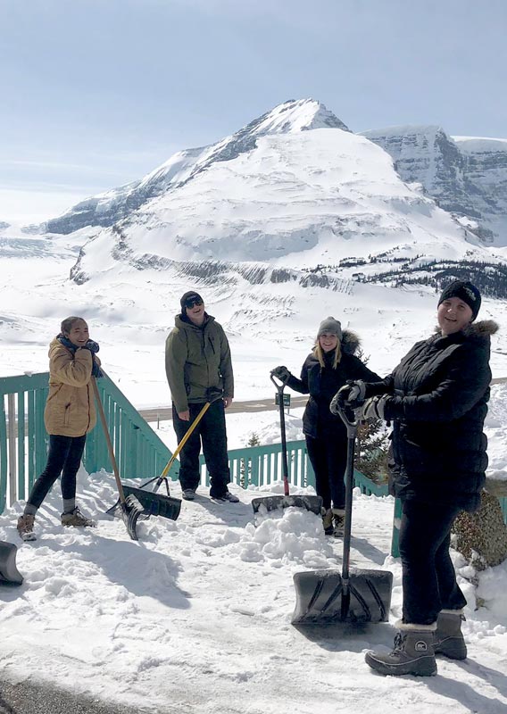 Five workers stand on a footpath with shovels. A large icefield and mountains in view