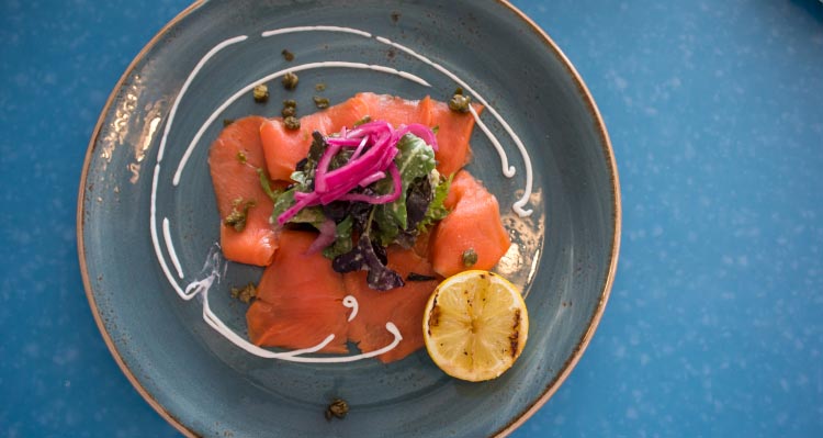 A plate of smoked salmon served with capers, lemon and salad.