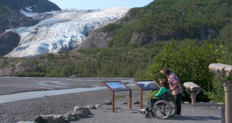 A person in a wheelchair looks out towards a large glacier.