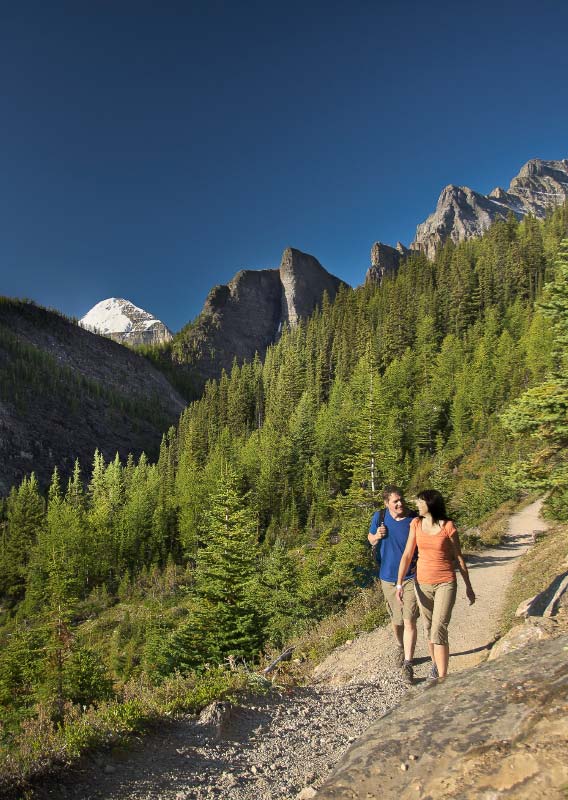 Two hikers walk along a mountainside trail.