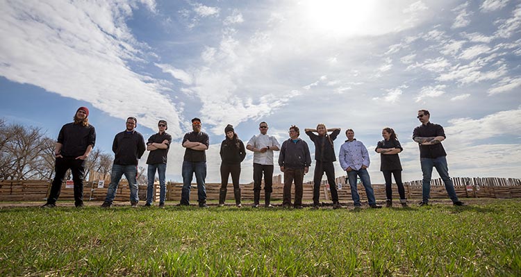 A group of chefs and farmers stand in an open field.