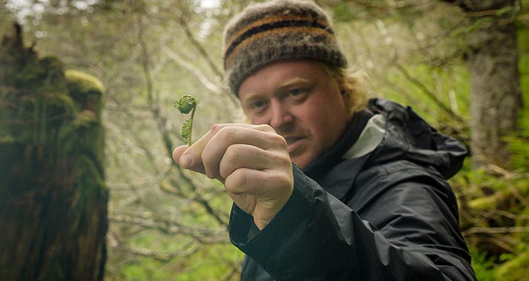 A man holds a fiddlehead up to the camera