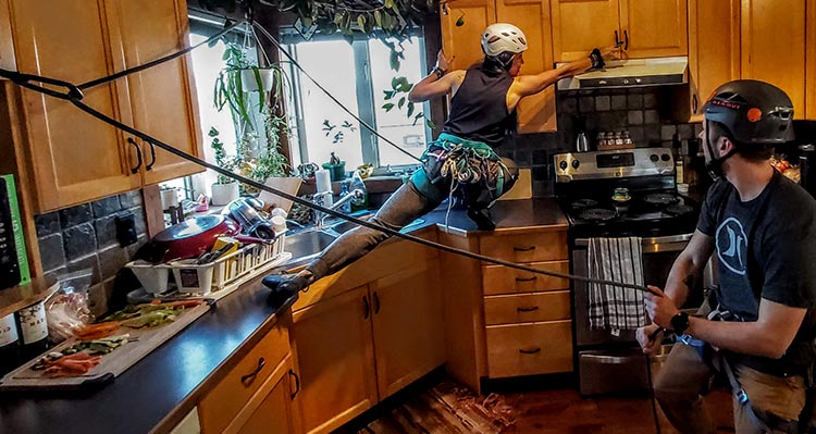 Two people use climbing equipment to climb around a kitchen.