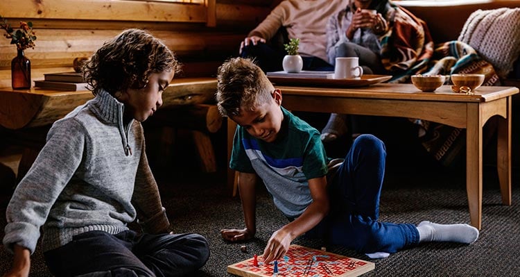Two kids play a board game in a cabin living room.