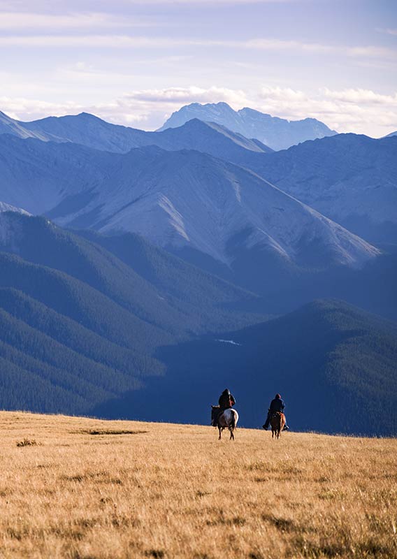 Two people on horseback in the distance on a mountain range.