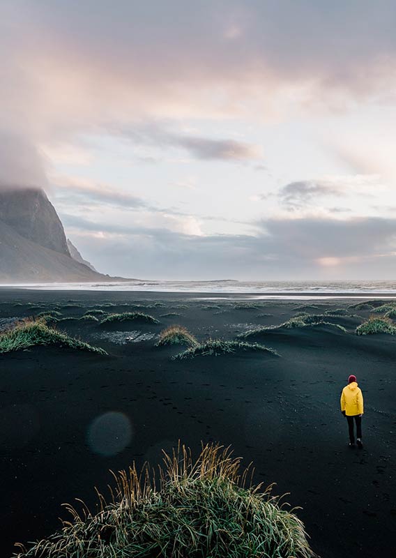 A man in a yellow jacket walks along a misty mountain shoreline.